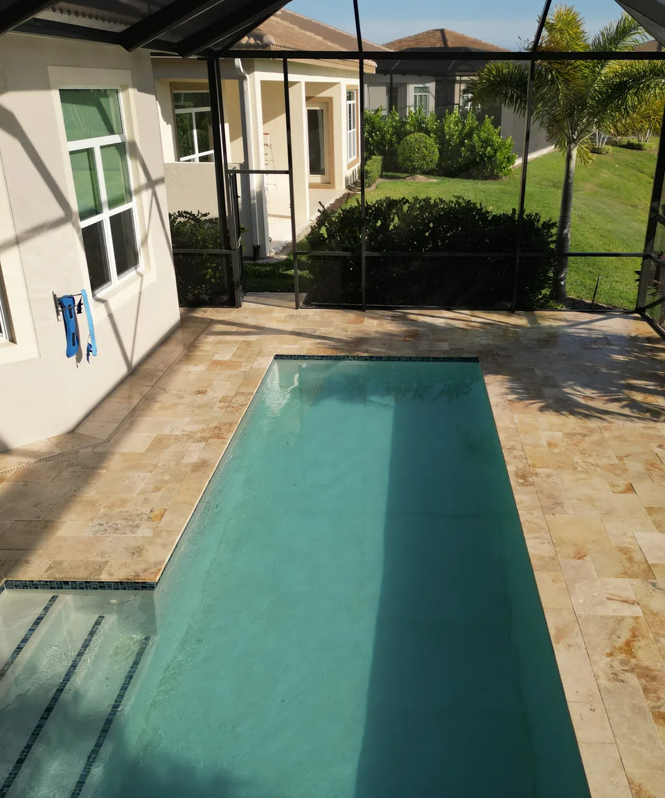 Travertine pool deck beside a home and screened lanai