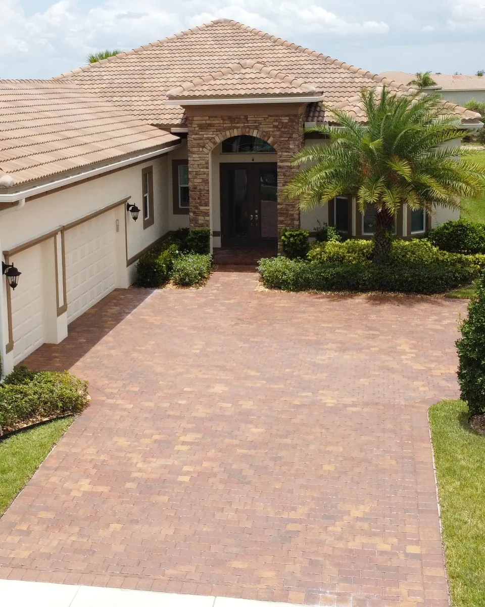 Paver driveway beside a stucco home and palms
